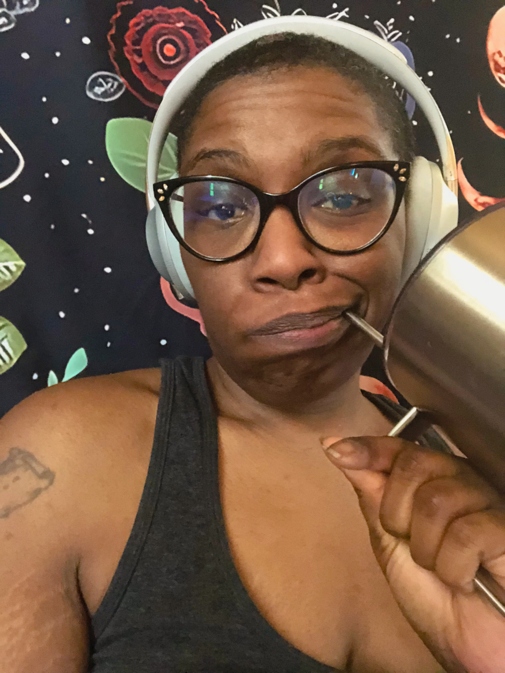 Sasha, a dark skinned person wearing a deep gray tank top, drinks water from a stainless steel tumbler.
