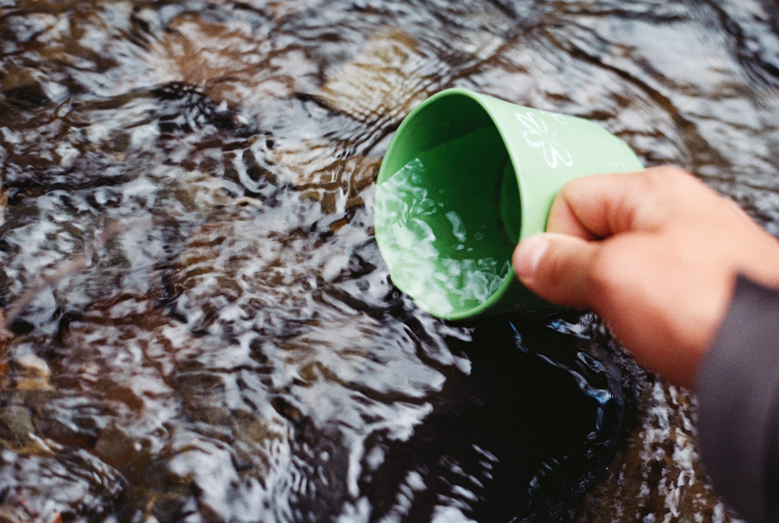 green coffee mug being dipped into a flowing stream