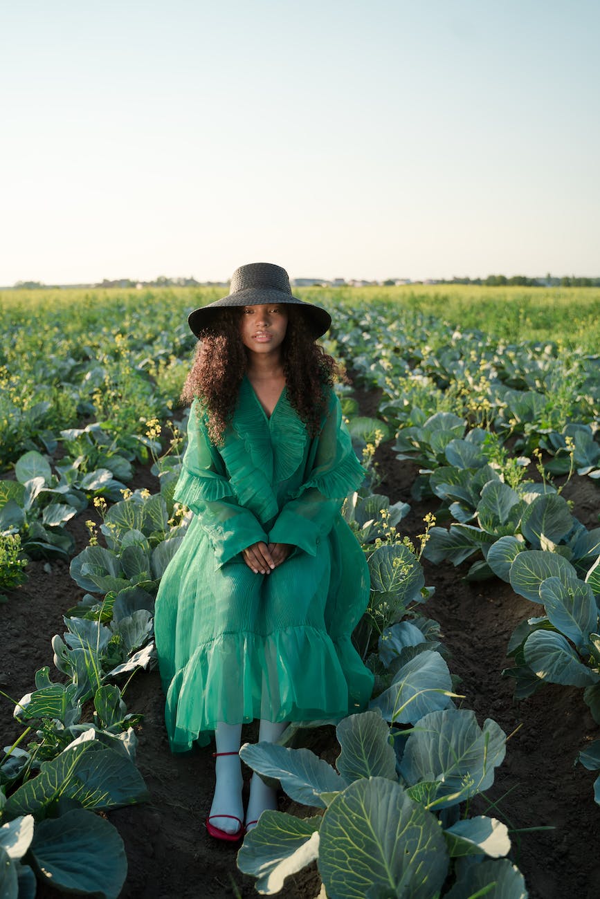 woman in green dress and wide brim hat sitting in cabbage field